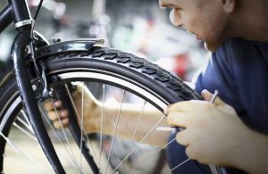 Mid-aged caucasian man making sure that the front wheel is aligned and balanced.Also checking if the brake is ok.Usual daily routine in bike workshop.He's wearing navy blue sweater.